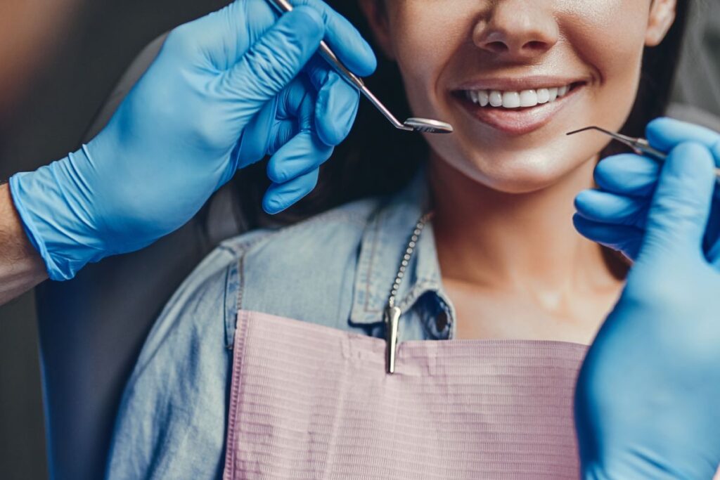 Dentist wearing blue gloves examines a patient’s teeth during a routine oral checkup.