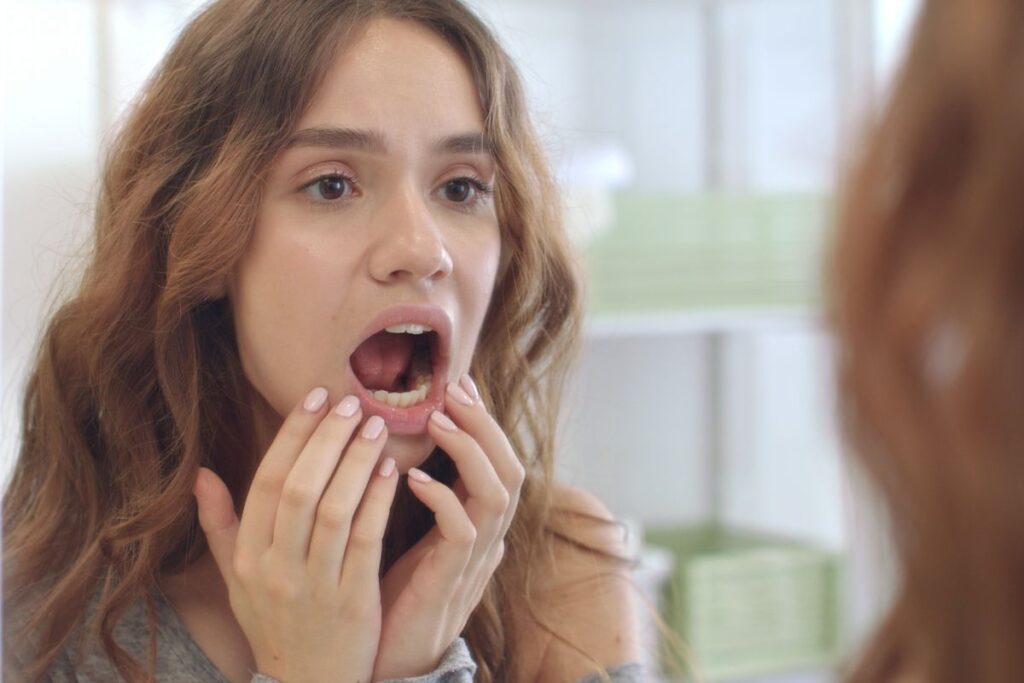 Woman examining her mouth in the mirror, checking for oral health issues.