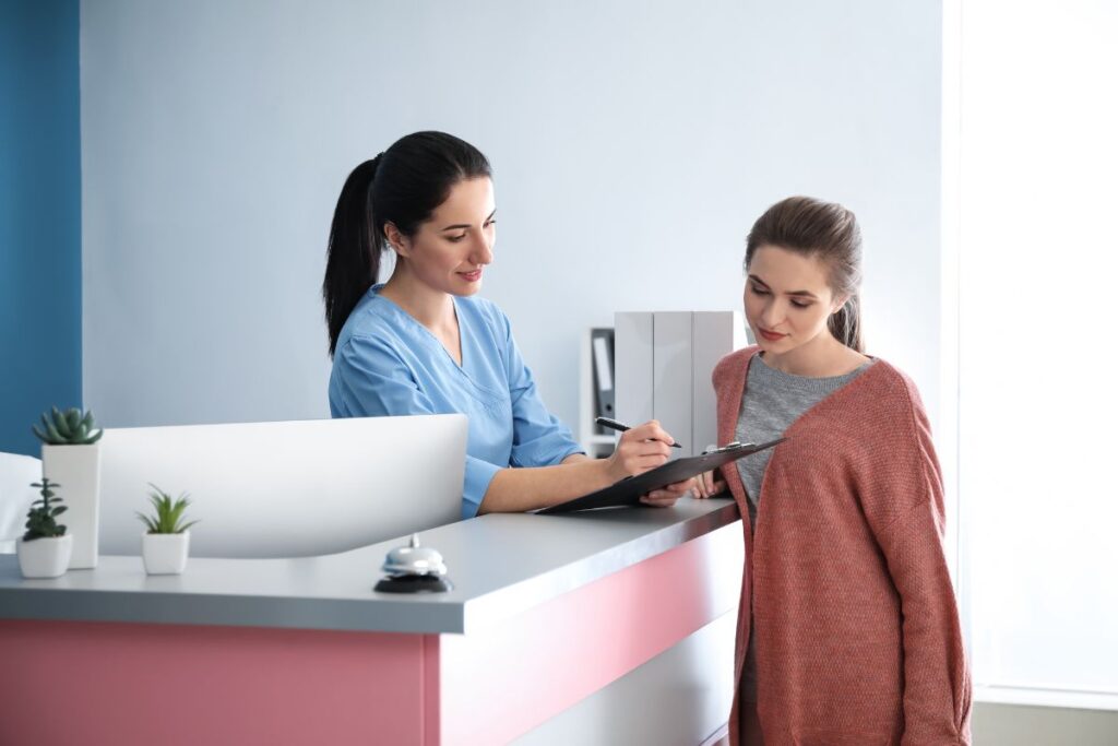 Receptionist assisting a patient with forms at a dental office front desk, creating a welcoming first-visit experience.