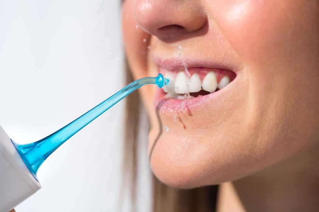 Close-up of a woman using a water flosser to clean between her teeth, with water visibly spraying.