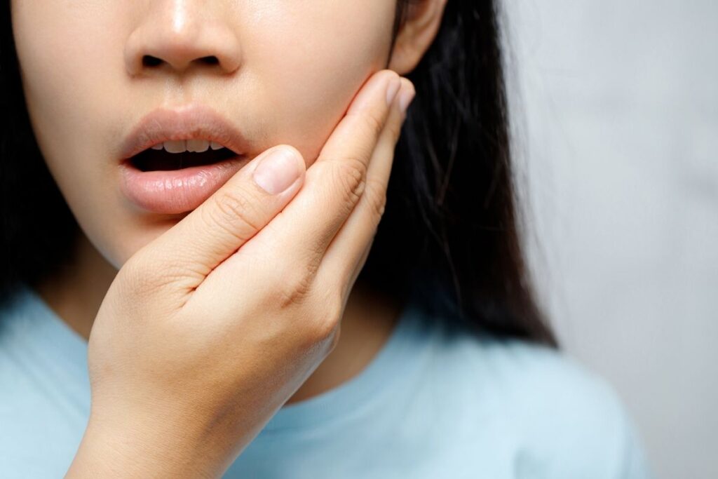 Woman holding her cheek in discomfort, indicating possible gum disease or oral inflammation.