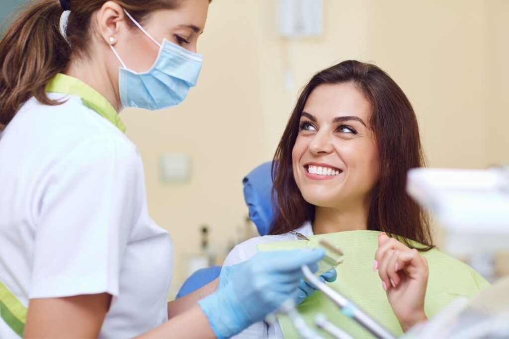 Smiling woman talks with masked dental hygienist during a routine visit, highlighting stress-free dental care.