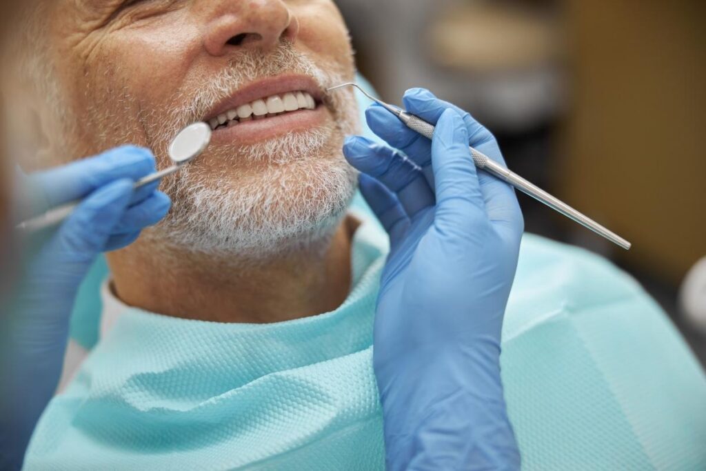 A dental professional wearing blue gloves holds a metal dental tool near a patient's mouth during an exam.