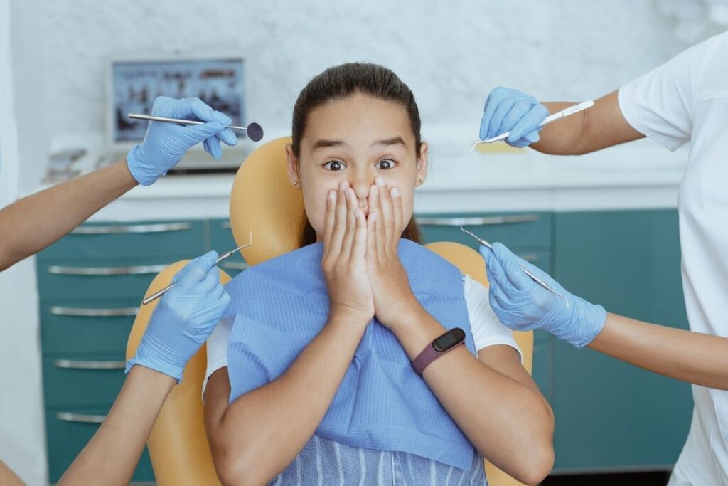 Dental professionals with blue gloves hold instruments near a patient seated in a dental clinic.