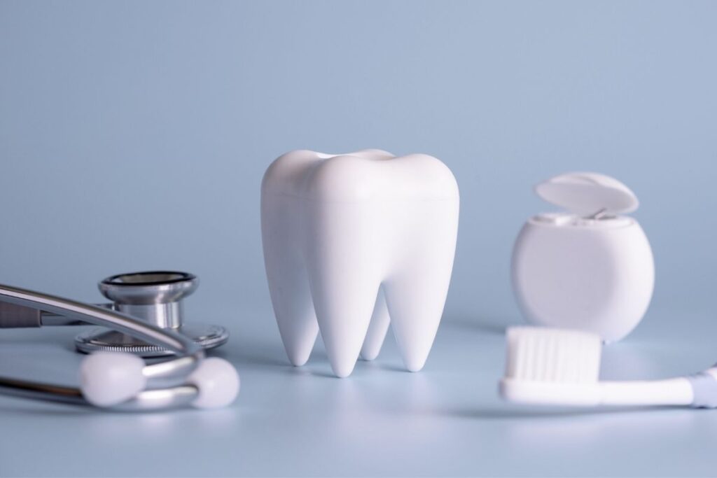 A large model of a tooth surrounded by a stethoscope, dental floss, and a toothbrush on a light blue background.