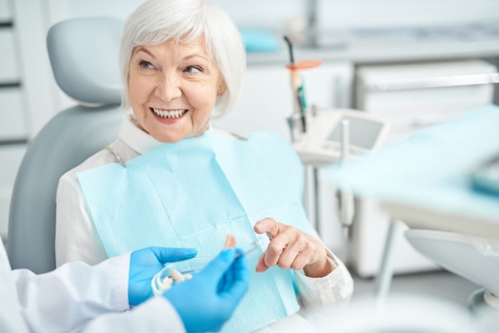 Elderly patient in a dental chair discusses dental models with a gloved dentist in a modern clinic setting.