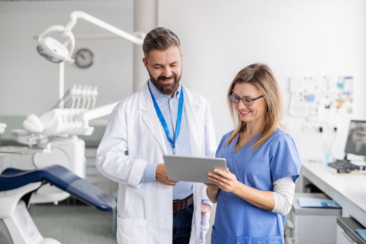 Smiling dental professionals discussing data on a tablet in a clean, well-equipped dental office.