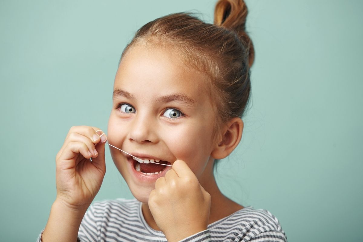 Close-up of a young girl flossing; open mouth and floss string held between both hands.