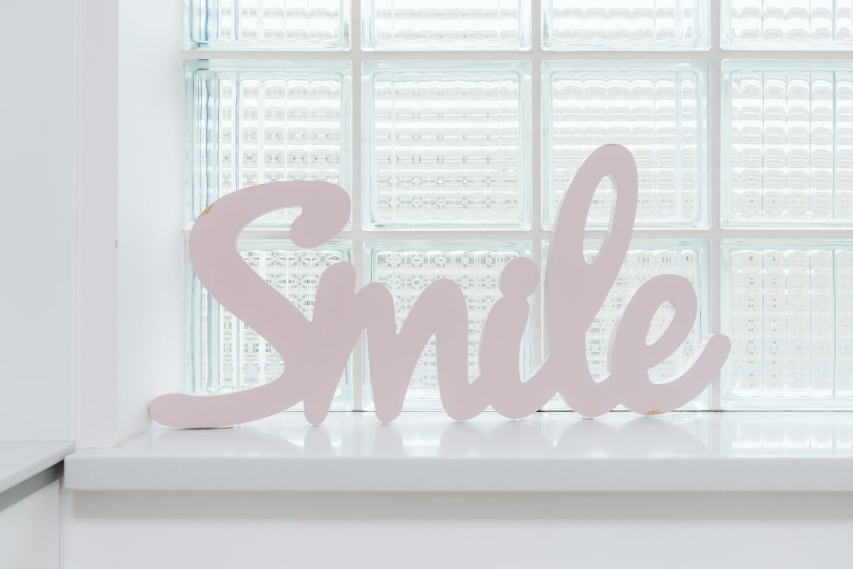 Decorative word ‘Smile’ in pale pink cursive, resting on a sill against frosted glass blocks.
