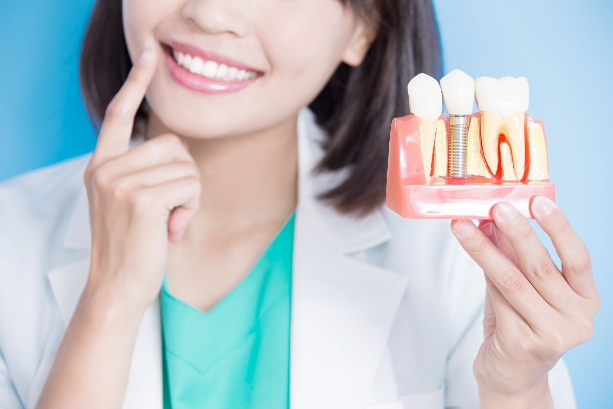 Close-up of a dental professional displaying a tooth implant model next to a healthy smile.